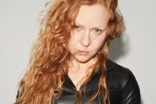 Photo of a woman with red curly hair and a black jacket.