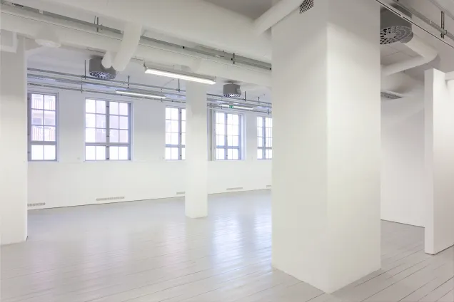 Vitmålad galleri med stora fönster. Foto.