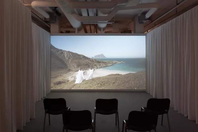 En filmvisning i ett galleri med draperade väggar. Foto.