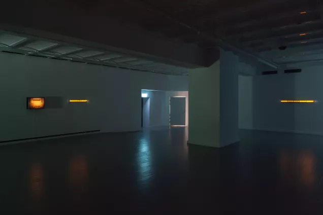 En mörklagt galleri med ljusboxar som lyser vagt i mörkret. Foto.